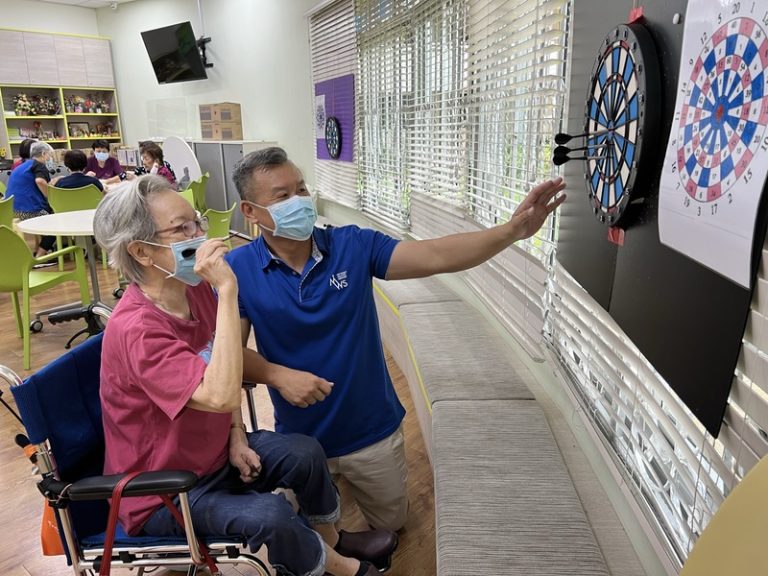 Brendon Yam guiding a senior in adaptive darts